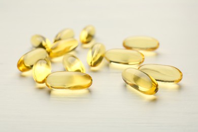 Yellow vitamin capsules on white wooden table, closeup