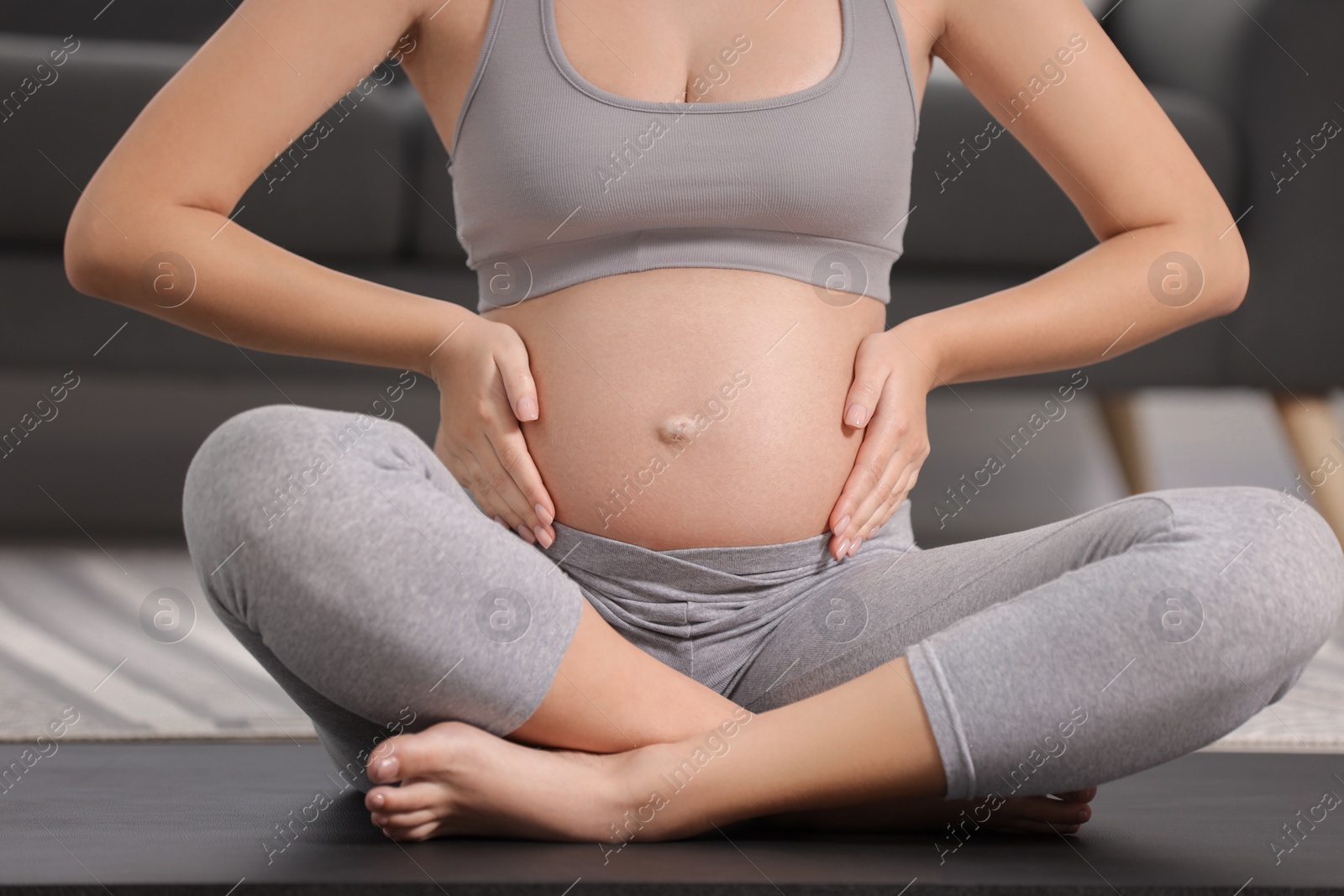 Photo of Pregnant woman sitting on yoga mat at home, closeup