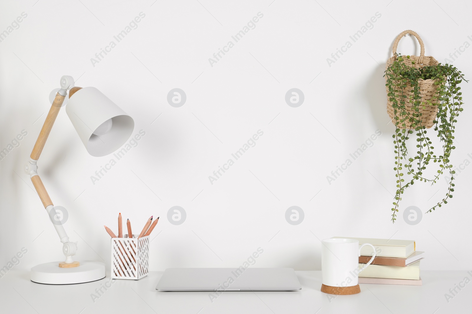 Photo of Cozy workspace with laptop, lamp and stationery on white desk at home