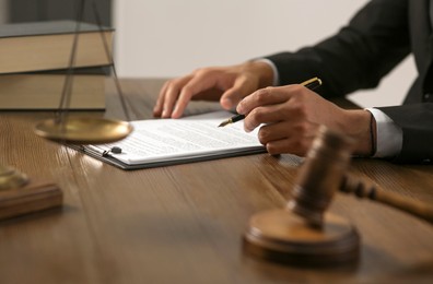 Photo of Law and justice. Closeup of judge working at wooden table near gavel