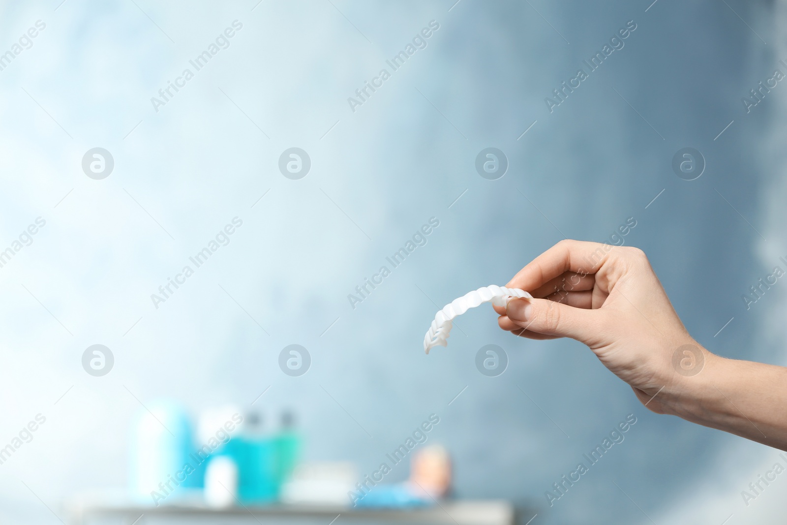 Photo of Dentist holding teeth cover in hand on blurred background. Space for text