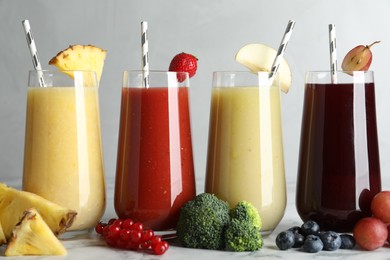 Glasses of delicious juices and fresh ingredients on white marble table