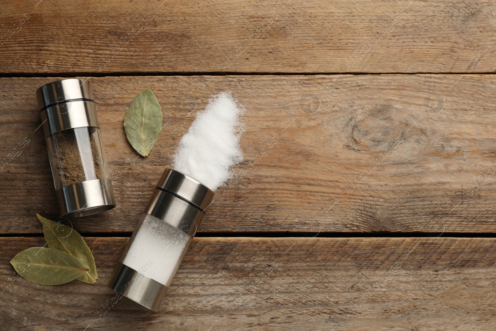 Photo of Salt and pepper shakers with bay leaves on wooden table, flat lay. Space for text