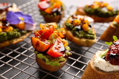 Delicious bruschettas with different toppings and balsamic vinegar on cooling rack, closeup