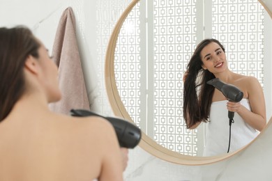 Photo of Beautiful young woman using hairdryer in bathroom