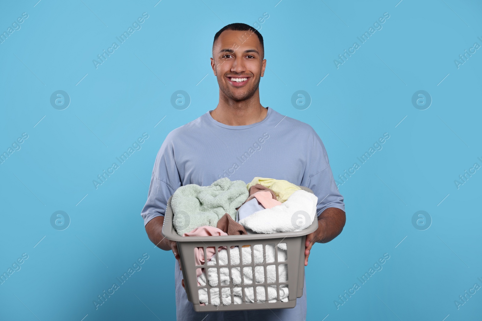 Photo of Happy man with basket full of laundry on light blue background