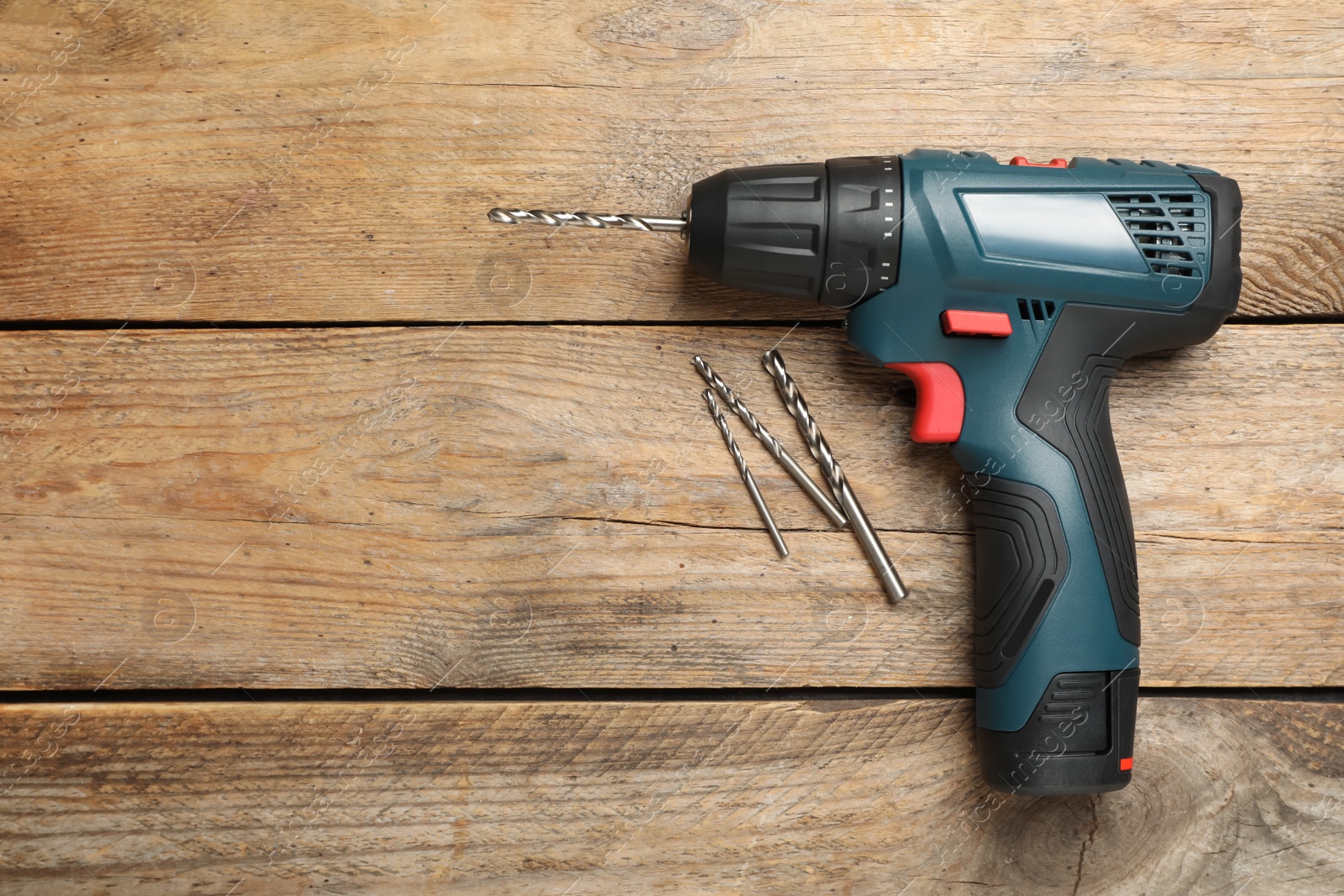 Photo of Modern electric power drill with bits on wooden table, flat lay. Space for text