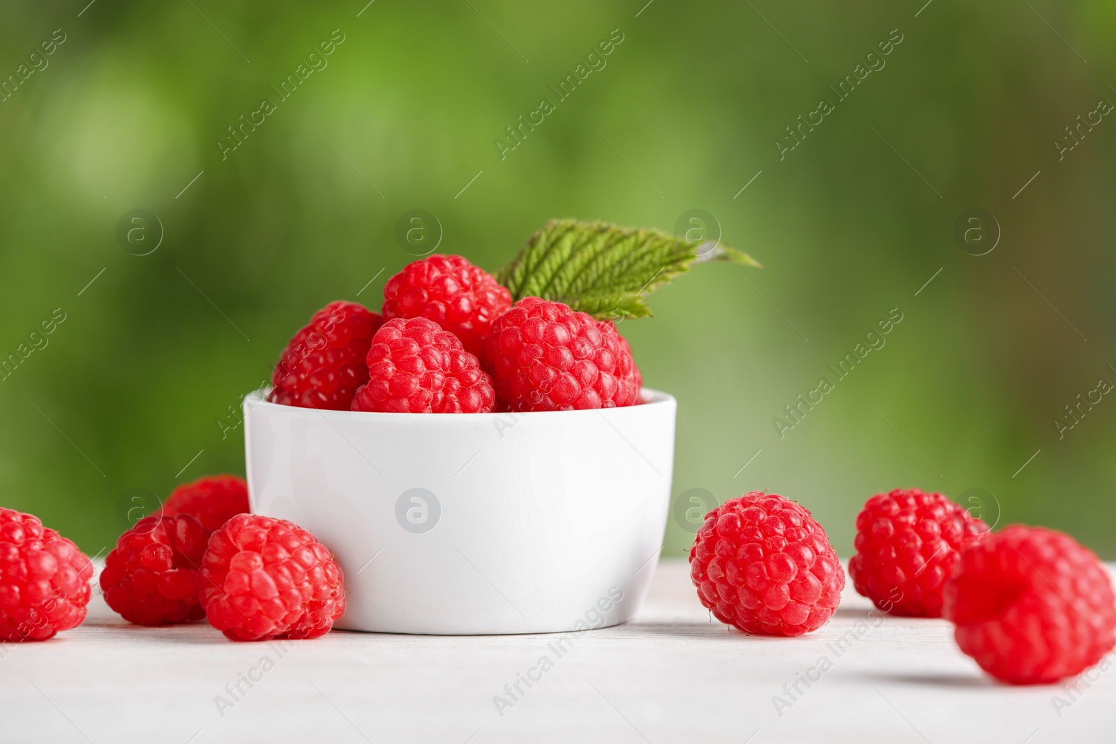 Photo of Tasty ripe raspberries and green leaf on white table outdoors