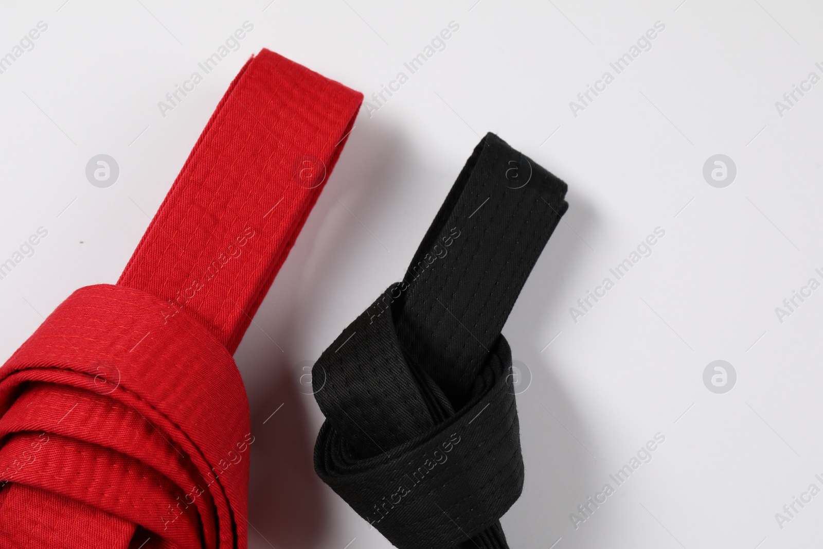 Photo of Red and black karate belts on white background, flat lay. Space for text