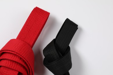 Photo of Red and black karate belts on white background, flat lay. Space for text