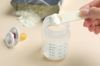 Woman preparing infant formula on beige background, closeup. Baby milk