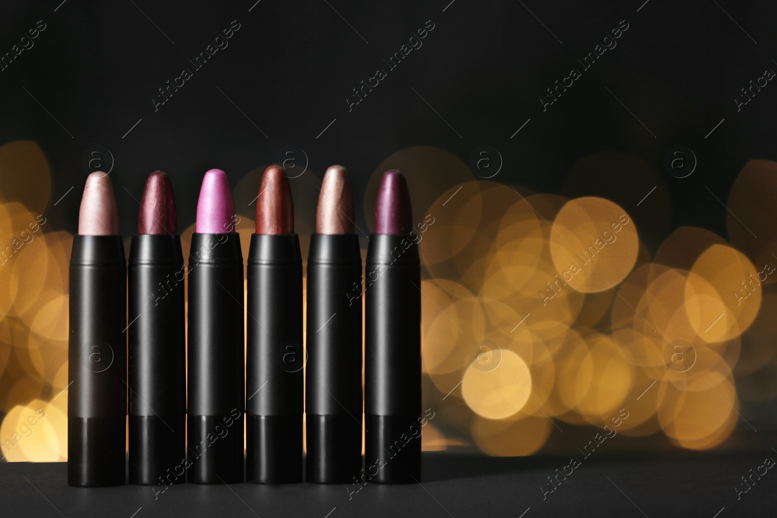 Photo of Set of bright lipsticks on table against blurred lights, space for text