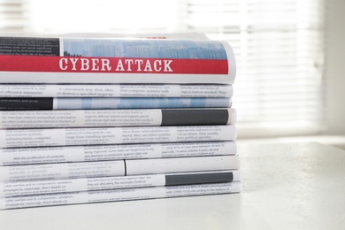 Newspapers with headline CYBER ATTACK stacked on white table indoors