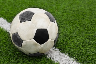 Dirty soccer ball on green football field, closeup