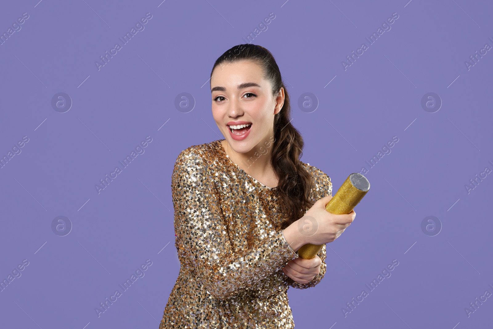 Photo of Young woman blowing up party popper on purple background, space for text