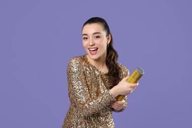 Photo of Young woman blowing up party popper on purple background, space for text