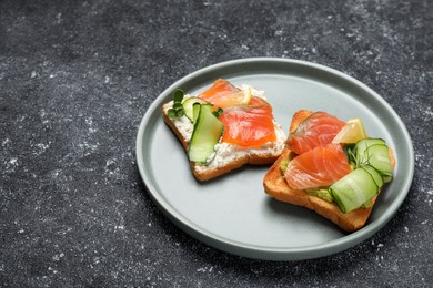 Photo of Tasty toasts with salmon, cream cheese and cucumber on grey table