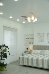 Photo of Comfortable furniture, ceiling fan, houseplants and accessories in stylish bedroom