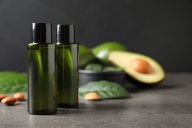 Bottles of avocado essential oil and almonds on grey table, closeup. Space for text