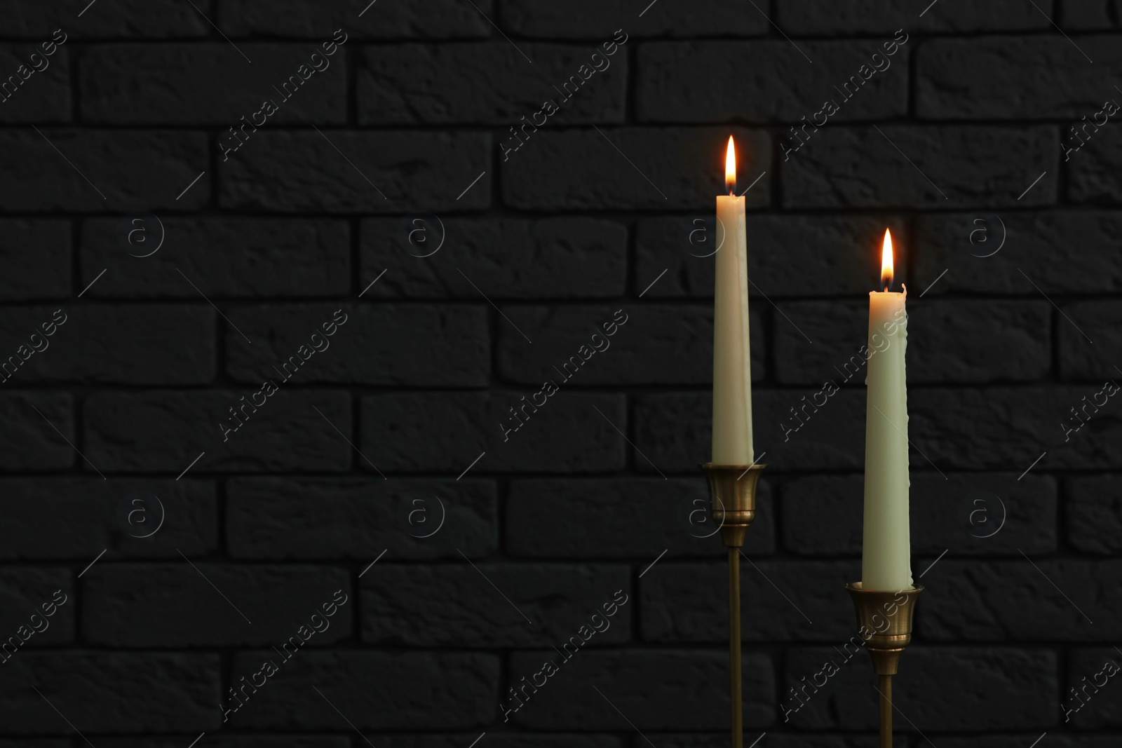 Photo of Burning candles near white brick wall in darkness, space for text