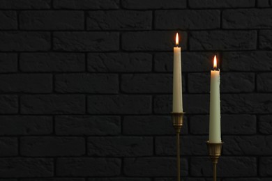 Photo of Burning candles near white brick wall in darkness, space for text