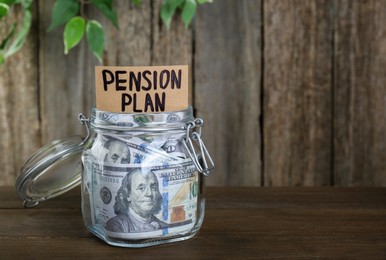Card with phrase Pension Plan and dollar banknotes in glass jar on wooden table, space for text. Retirement concept