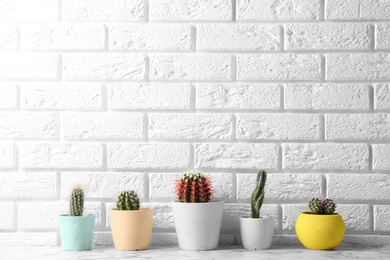 Photo of Different potted cacti on table near brick wall, space for text. Interior decor