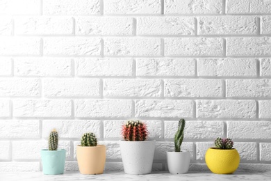 Different potted cacti on table near brick wall, space for text. Interior decor