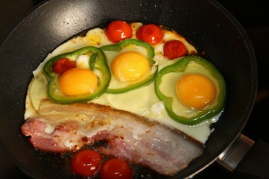 Photo of Cooking eggs with bacon, tomatoes and pepper in frying pan, closeup
