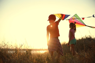 Photo of Little children playing with kites outdoors at sunset. Spending time in nature