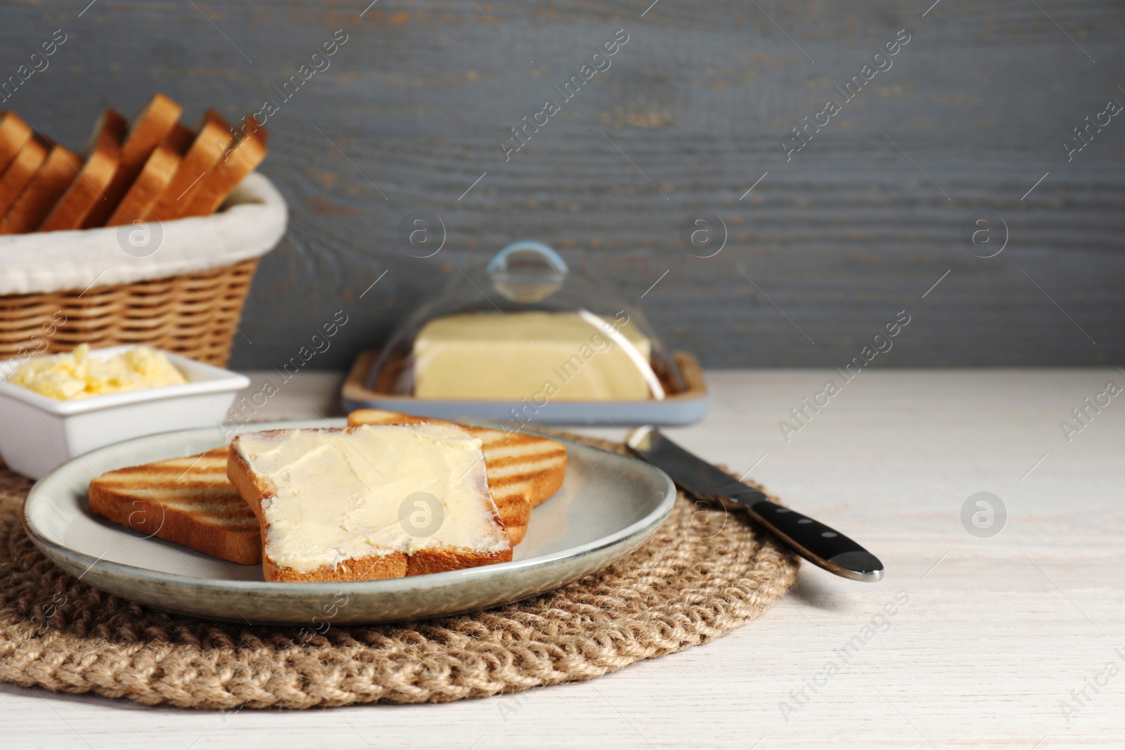 Photo of Tasty toasts served with butter on white wooden table. Space for text