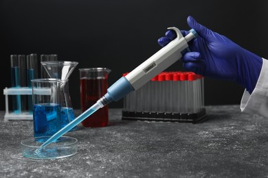 Photo of Laboratory analysis. Scientist dripping sample with micropipette into petri dish at grey table, closeup