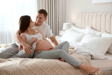 Photo of Young pregnant woman with her husband in bedroom