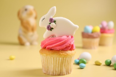 Tasty cupcake with Easter decor on pale yellow background, closeup