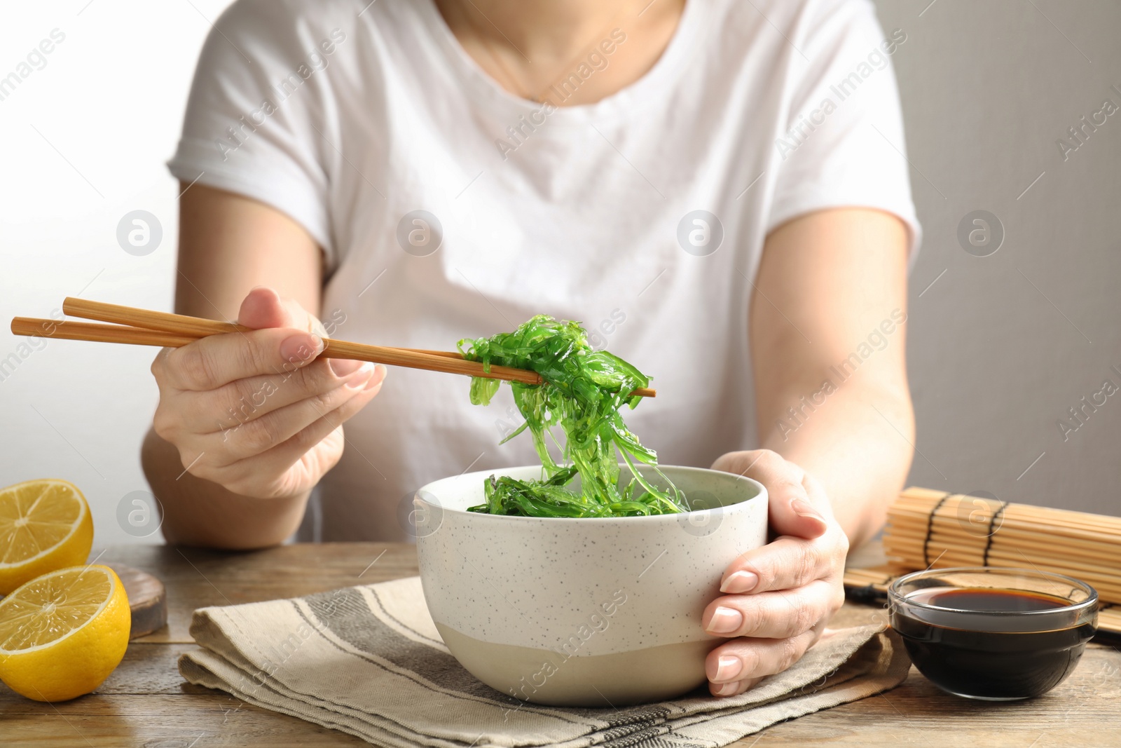 Photo of Woman eating Japanese seaweed salad at table, closeup