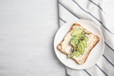 Slice of bread with spread and avocado on white wooden table, flat lay. Space for text