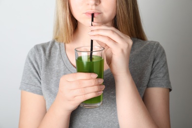 Woman drinking spirulina shake from glass on grey background, closeup
