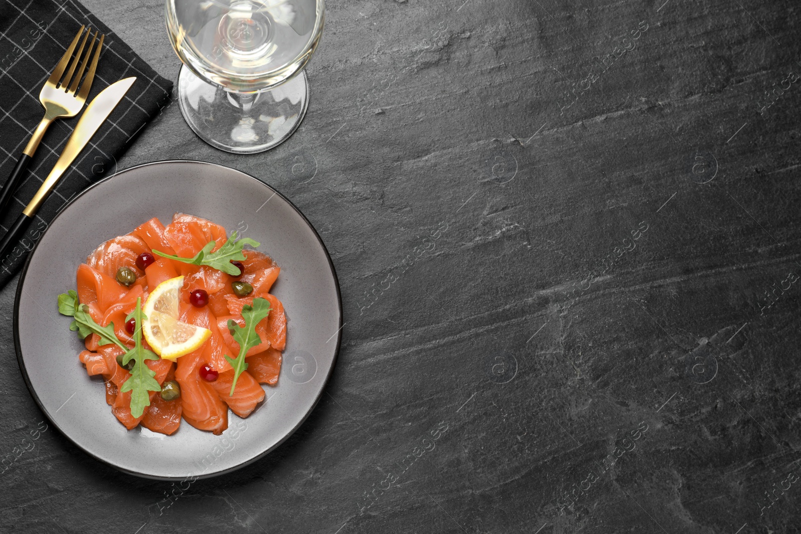 Photo of Salmon carpaccio with capers, cranberries, arugula and lemon served on black table, flat lay. Space for text