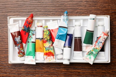 Photo of Pack of tubes with oil paints on wooden table, top view