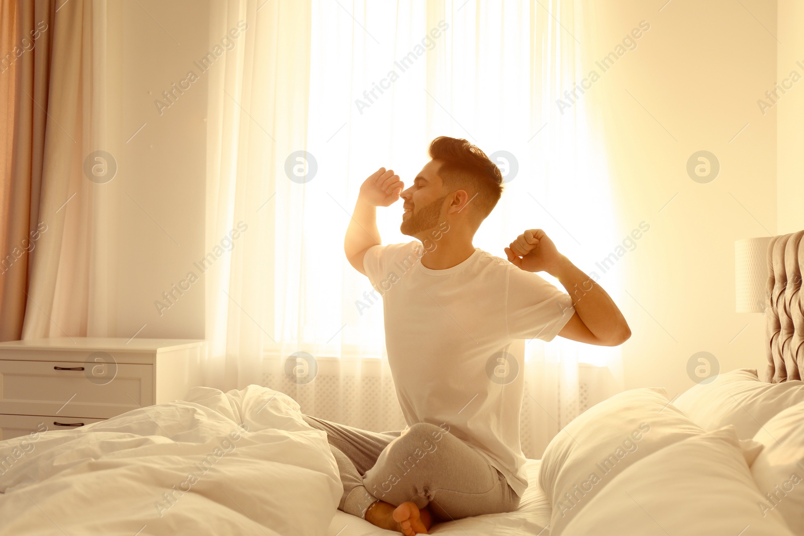 Photo of Young man stretching on bed at home. Lazy morning