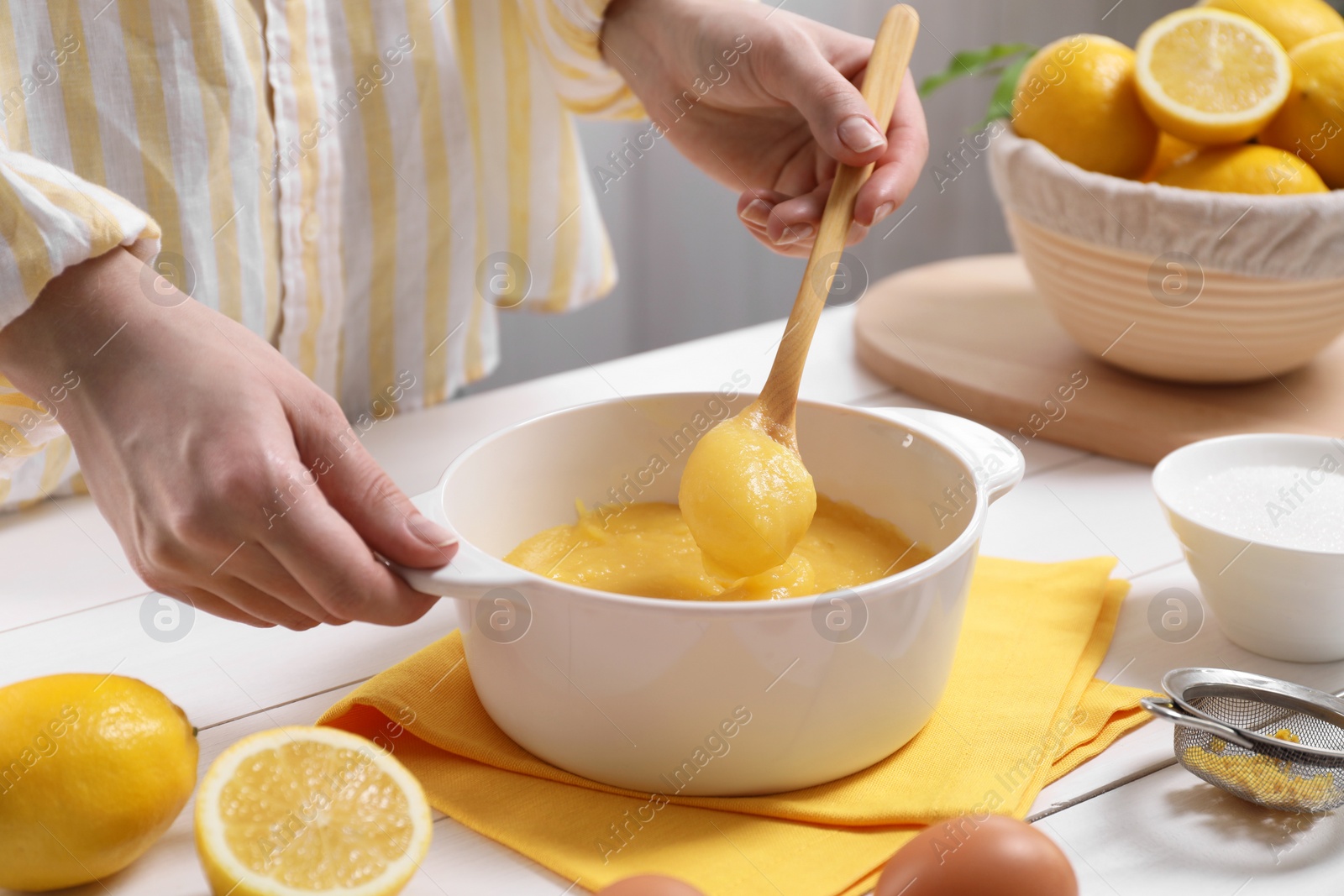 Photo of Woman cooking lemon curd at white wooden table, closeup