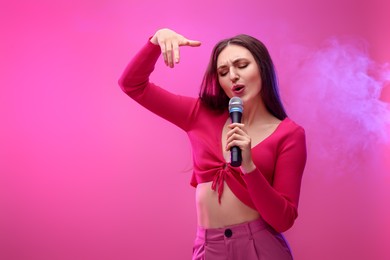 Photo of Emotional woman with microphone singing on pink background. Space for text