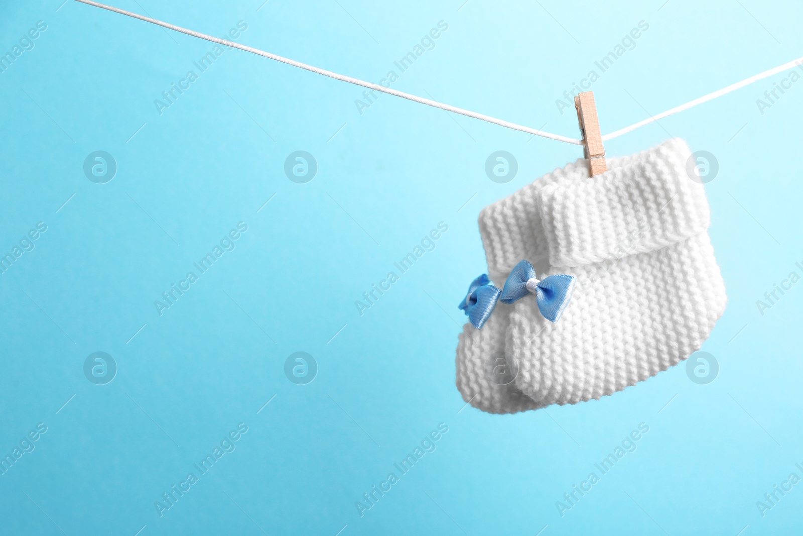 Photo of Knitted booties hanging on washing line against color background, space for text. Baby accessories