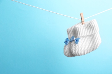 Photo of Knitted booties hanging on washing line against color background, space for text. Baby accessories