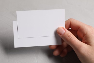 Woman holding blank cards at light grey table, closeup. Mockup for design