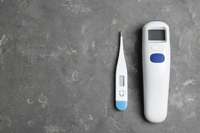 Photo of Non-contact infrared and digital thermometers on grey stone background, flat lay. Space for text