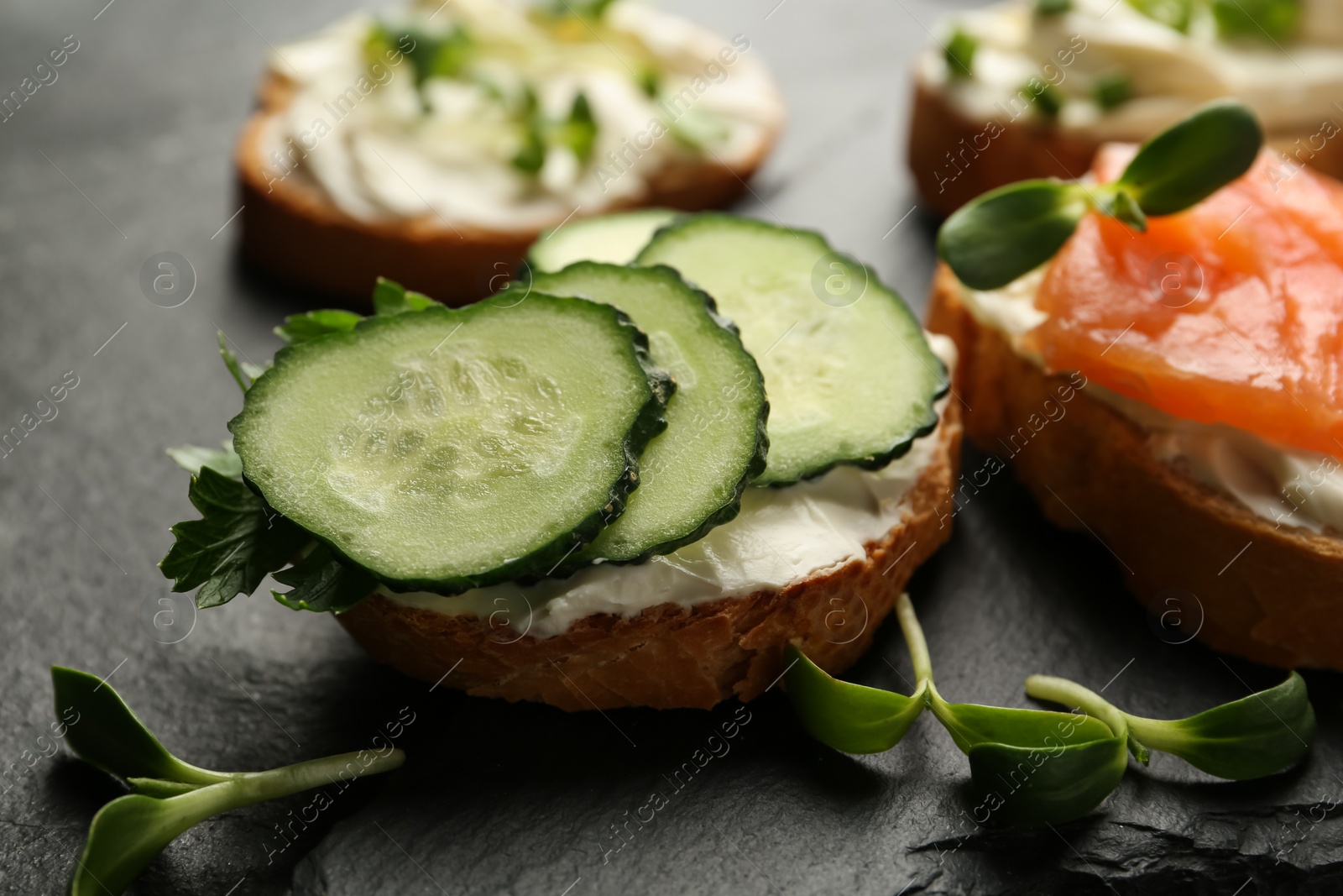 Photo of Delicious sandwiches with cream cheese and other ingredients on black table, closeup