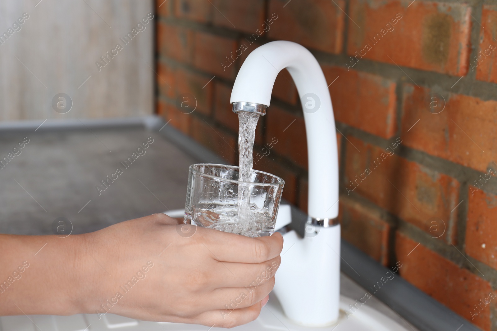 Photo of Woman filling glass with water from faucet in kitchen, closeup