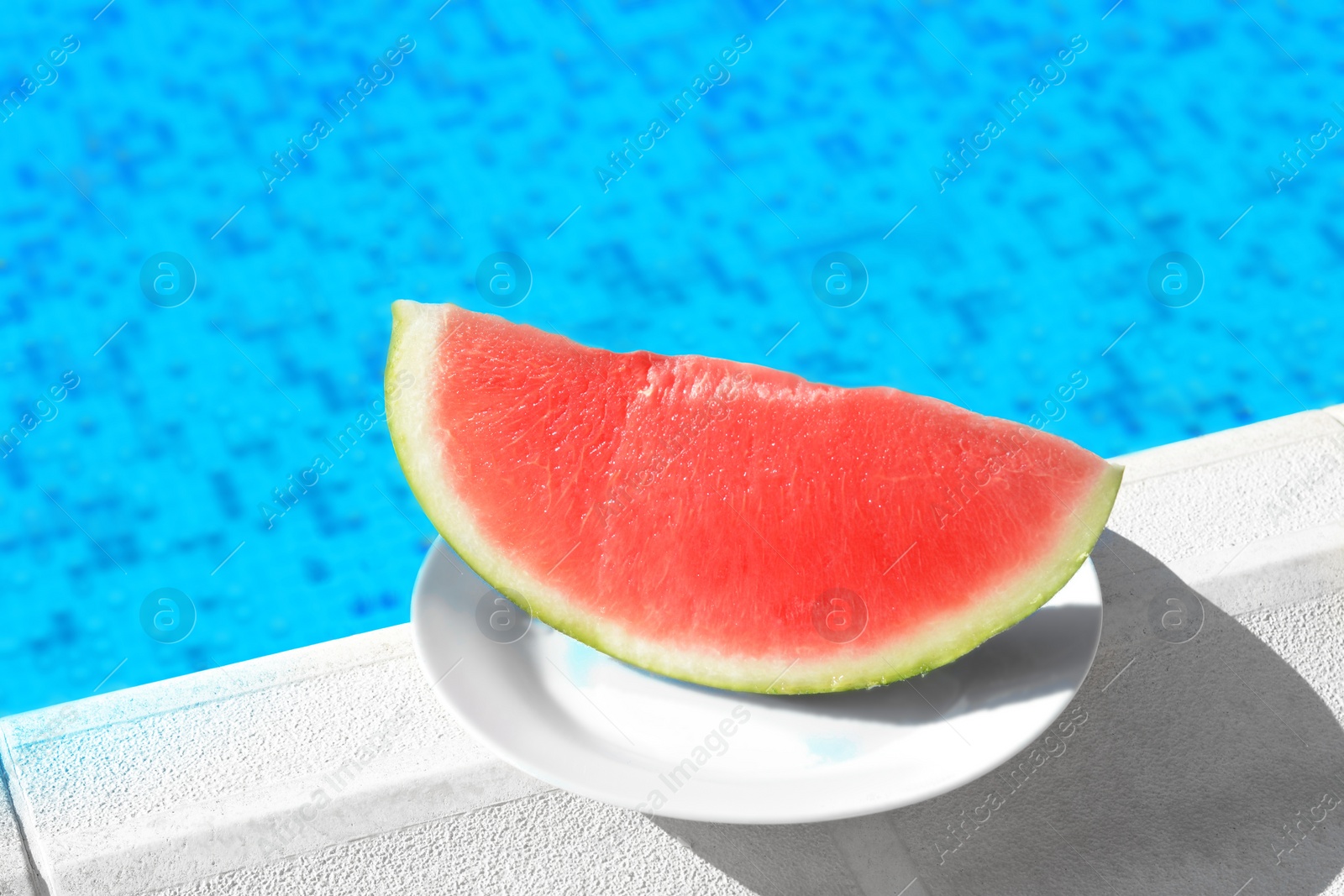 Photo of Slice of fresh juicy watermelon on white plate near swimming pool outdoors