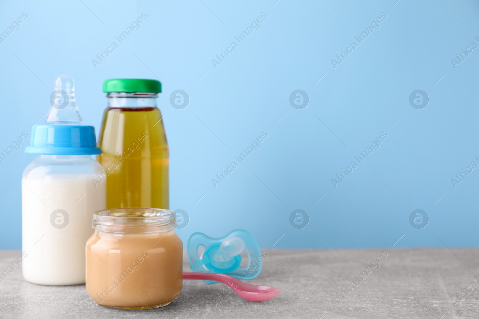 Photo of Jar with healthy baby food, milk, juice, pacifier and spoon on light grey table, space for text